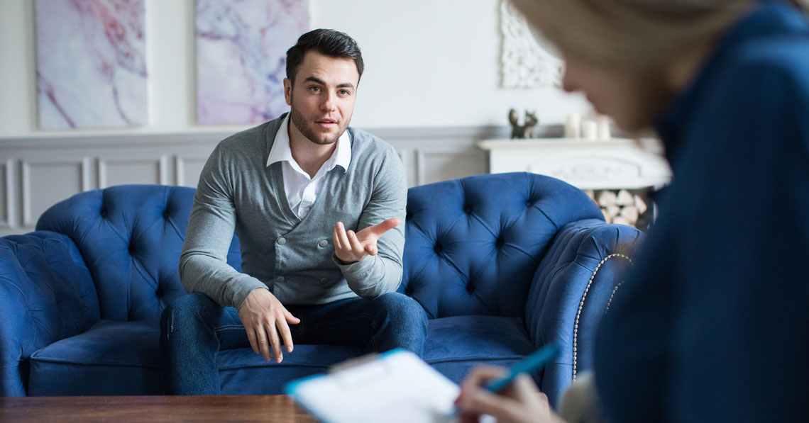Man sitting on a blue couch, talking to a therapist and gesturing with his hands