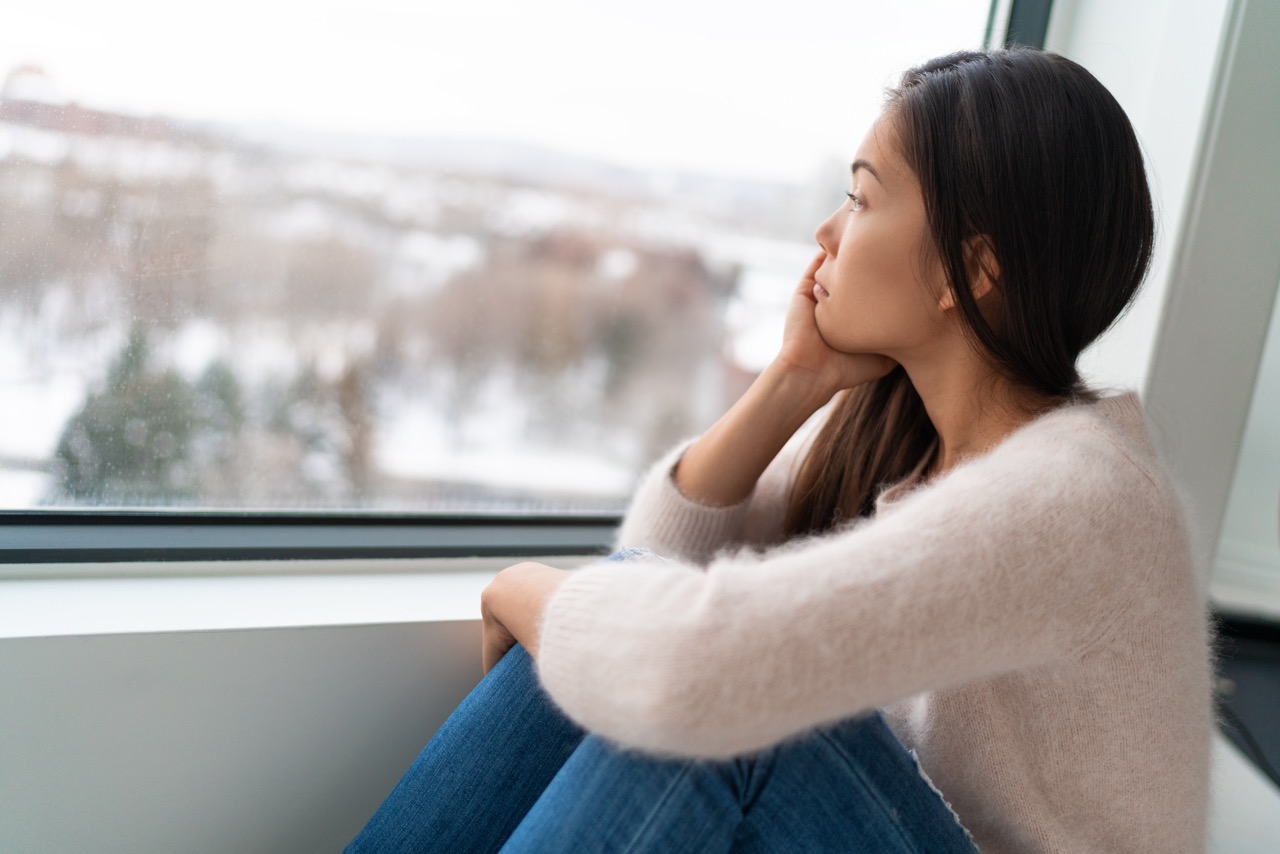 depressed girl looks out winter window